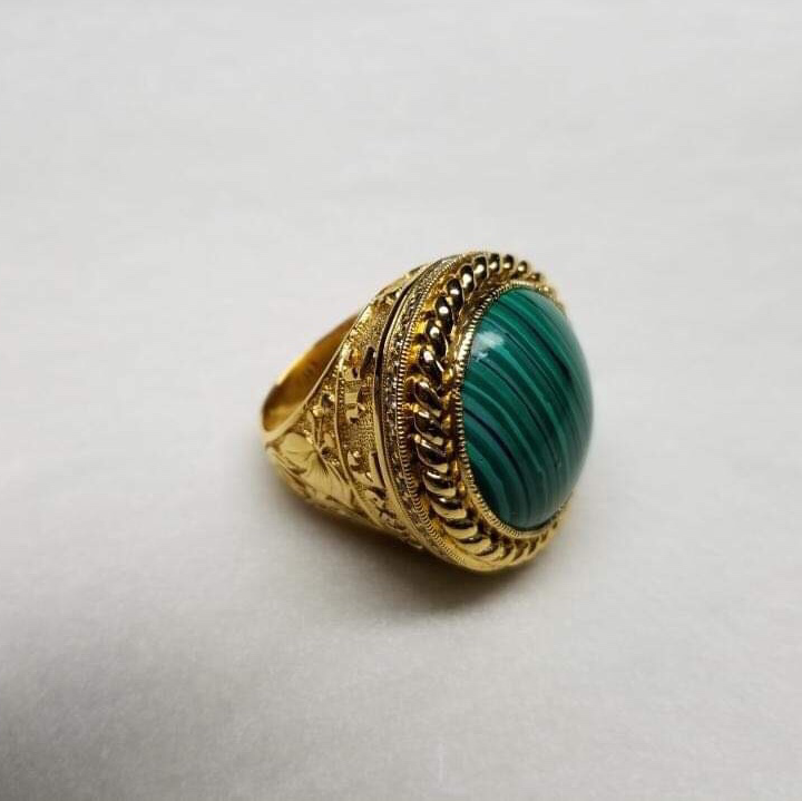 An ornate gold ring with a green stone and intricate sculpted details